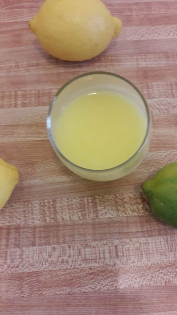Overhead view of lemon curd in a glass cup with a few lemons scattered around