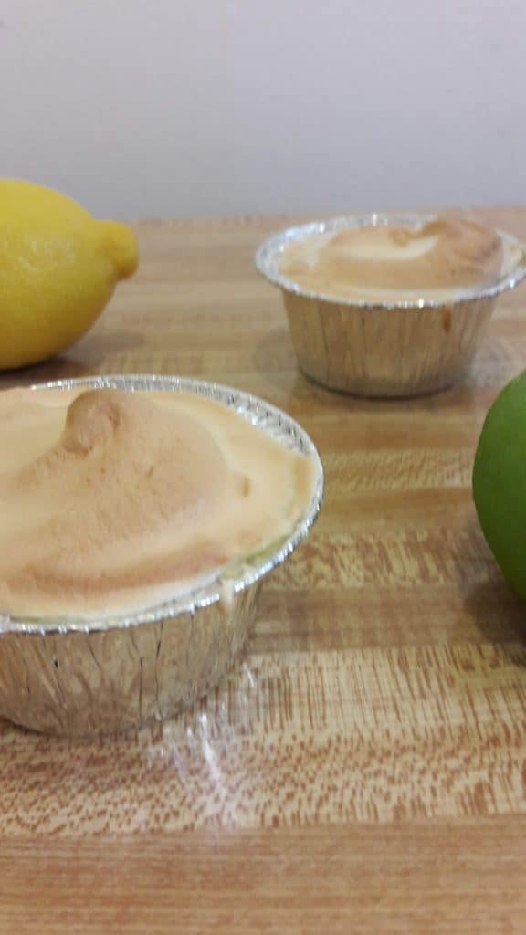 two mini lemon meringue pie cups and two lemons on a table