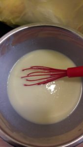 Bowl containing muffin batter and a red whisk