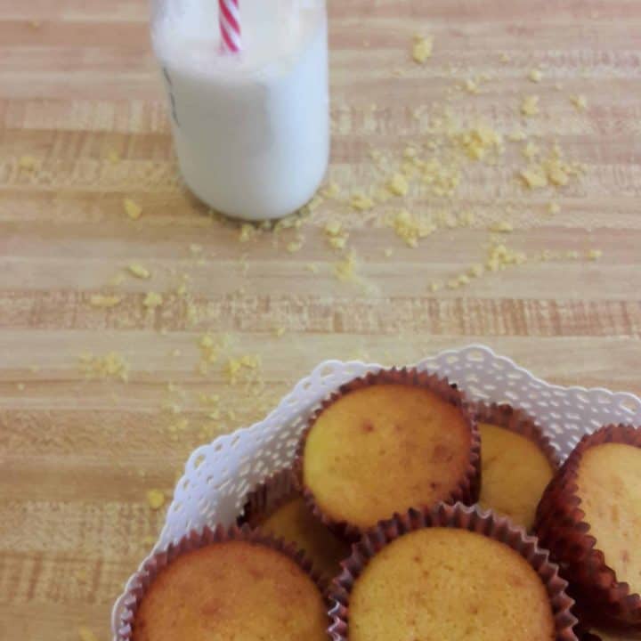 A bowl of sweet corn muffins in the foreground and a small glass jug of milk in the background