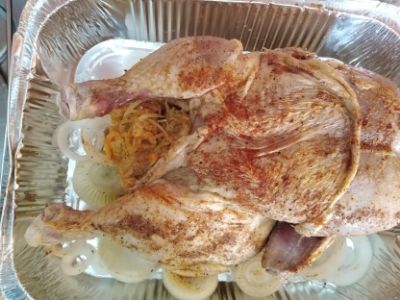 A whole chicken in a baking pan, with spices, onions, and stuffing.