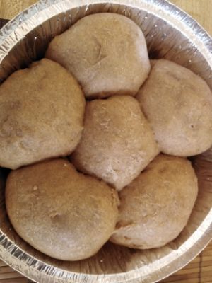 Small round baking pan with six much larger challah dough balls in it.